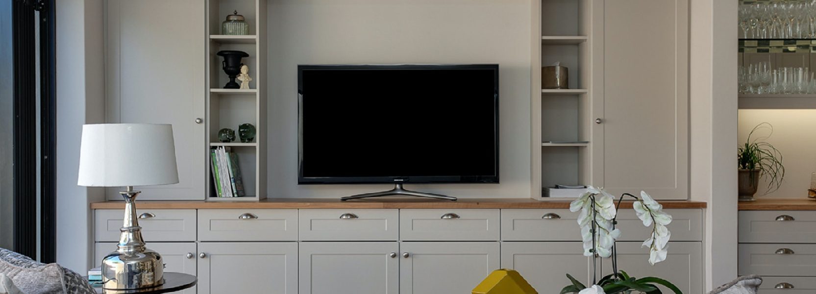 tv sitting on a tv stand in a living room surrounded by lamps and cupboards